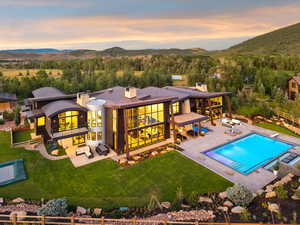 Back of house at dusk with an outdoor living space, a chimney, a balcony, a fenced backyard, and a patio