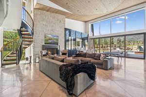 Living area featuring a towering ceiling, wood ceiling, stairway, a fireplace, and concrete flooring