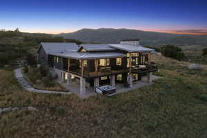 Back of house at dusk with stone siding, a chimney, a patio, a deck with mountain view, and a metal roof