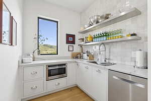 Kitchen with open shelves, decorative backsplash, stainless steel dishwasher, and white cabinets