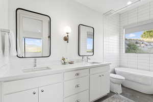 Full bath featuring plenty of natural light, a soaking tub, double vanity, and tile walls
