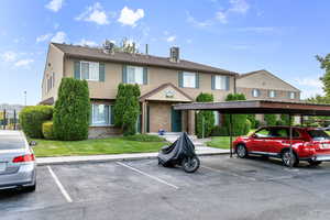 View of front of house featuring covered and uncovered parking, brick siding, and a front yard