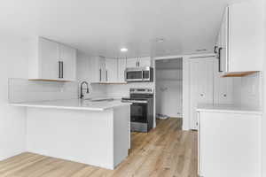 Kitchen featuring a peninsula, stainless steel appliances, backsplash, light wood-style flooring, and recessed lighting