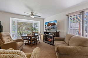 Living room featuring carpet flooring, a ceiling fan, plenty of natural light, and a glass covered fireplace