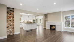 Unfurnished living room with dark wood-style floors, recessed lighting, and a warm lit fireplace