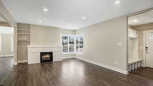 Unfurnished living room featuring dark wood-style flooring, recessed lighting, and a warm lit fireplace