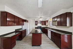 Kitchen featuring a ceiling fan, a textured ceiling, a kitchen island, light wood-type flooring, and white appliances