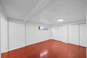 Unfurnished bedroom featuring multiple closets, wood finished floors, beamed ceiling, and a textured ceiling