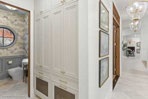 Hallway with a chandelier, wallpapered walls, a decorative wall, and wainscoting
