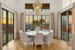 Dining room with french doors, a chandelier, light wood-style flooring, a towering ceiling, and a decorative wall
