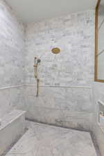 Full bath featuring tiled shower and tile walls