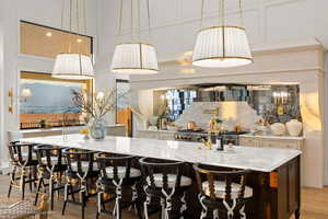 Kitchen featuring backsplash, light stone counters, hanging light fixtures, light wood finished floors, and a towering ceiling