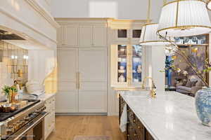 Kitchen featuring range with two ovens, light wood-style flooring, light stone counters, premium range hood, and glass insert cabinets