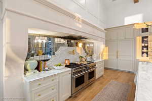 Kitchen featuring range with two ovens, decorative backsplash, glass insert cabinets, light wood-style floors, and light stone counters