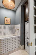 Washroom featuring stacked washing machine and dryer, light tile patterned flooring, and cabinet space