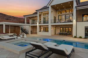 Rear view of house with an in-ground hot tub, a balcony, a mountain view, stucco siding, and a patio