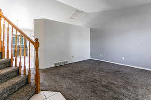 Empty room with light carpet, stairway, and lofted ceiling