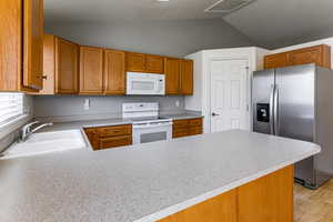 Kitchen featuring white appliances, vaulted ceiling, a peninsula, light countertops, and light wood-type flooring