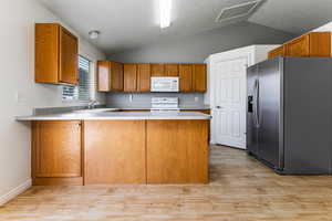 Kitchen with white appliances, vaulted ceiling, a peninsula, brown cabinets, and light countertops