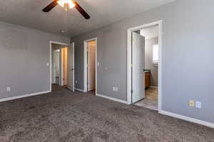 Primary bedroom with a textured ceiling, light colored carpet, ensuite bath, and a ceiling fan