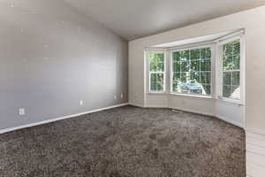 Carpeted empty room featuring lofted ceiling and baseboards