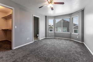 Primary bedroom with a textured ceiling, a spacious closet, carpet, connected bathroom, and ceiling fan