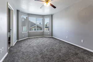 Primary bedroom carpeted empty room featuring a textured ceiling and a ceiling fan