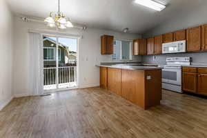 Kitchen with white appliances, a chandelier, a peninsula, brown cabinets, and light wood finished floors