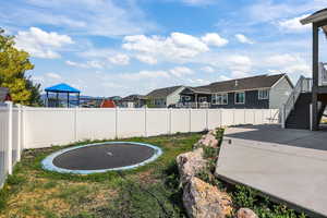 Fenced backyard featuring a trampoline, a residential view, stairs, and a patio area