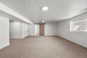 Below grade area featuring light carpet, a barn door, and a textured ceiling