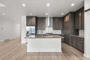 Kitchen featuring backsplash, dark brown cabinets, appliances with stainless steel finishes, wall chimney exhaust hood, and recessed lighting