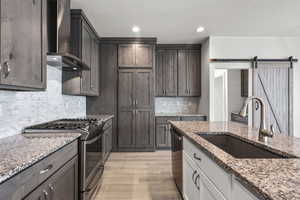 Kitchen with appliances with stainless steel finishes, wall chimney exhaust hood, light wood-style flooring, light stone countertops, and backsplash