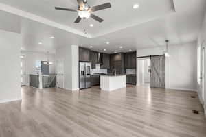 Unfurnished living room with a barn door, recessed lighting, light wood-style floors, ceiling fan, and a chandelier