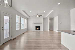Unfurnished living room with a raised ceiling, ceiling fan, light wood finished floors, recessed lighting, and a glass covered fireplace