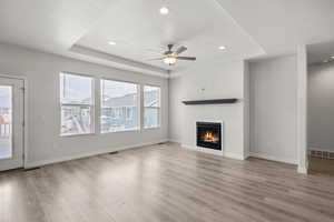 Unfurnished living room with a raised ceiling, a glass covered fireplace, ceiling fan, light wood-style floors, and recessed lighting