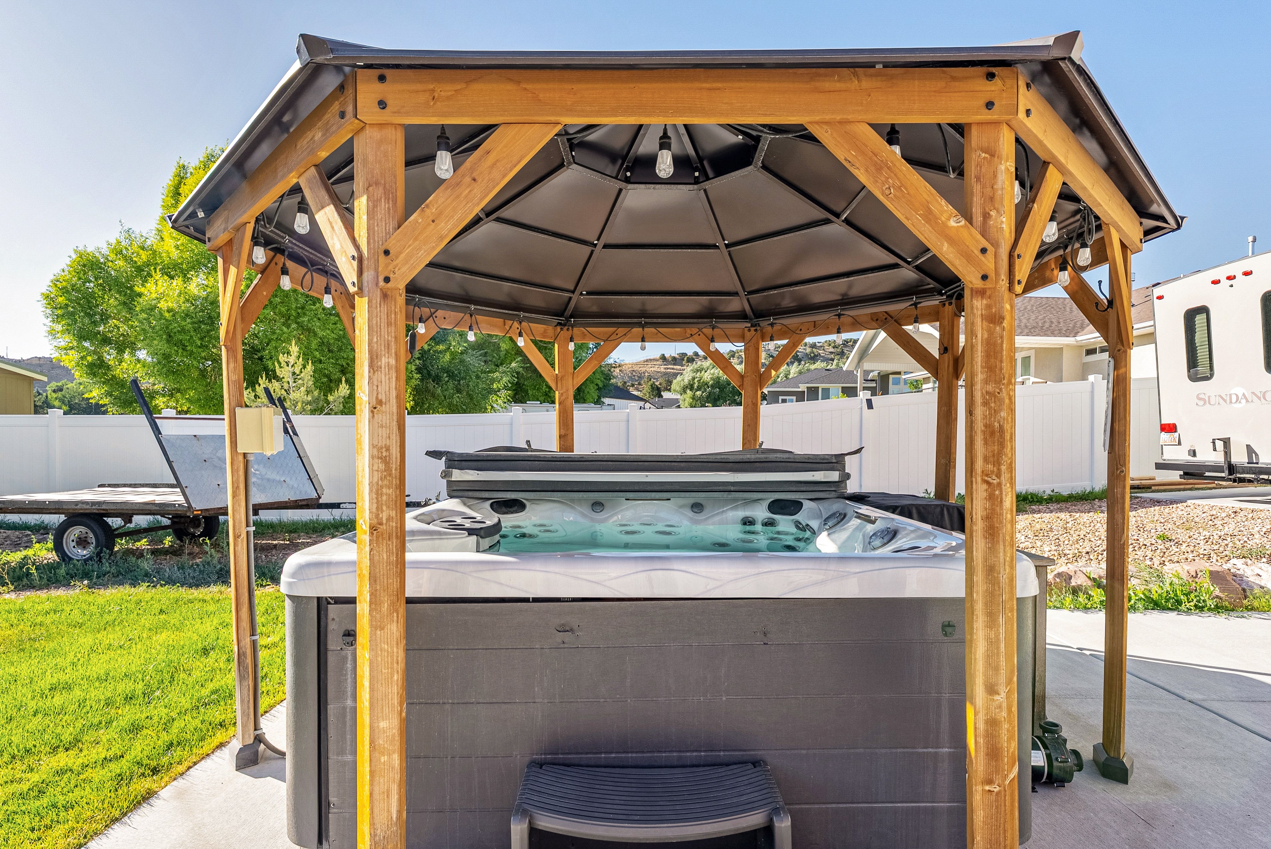 Outdoor hot tub set within a wood-frame gazebo, featuring a dark canopy and string lighting