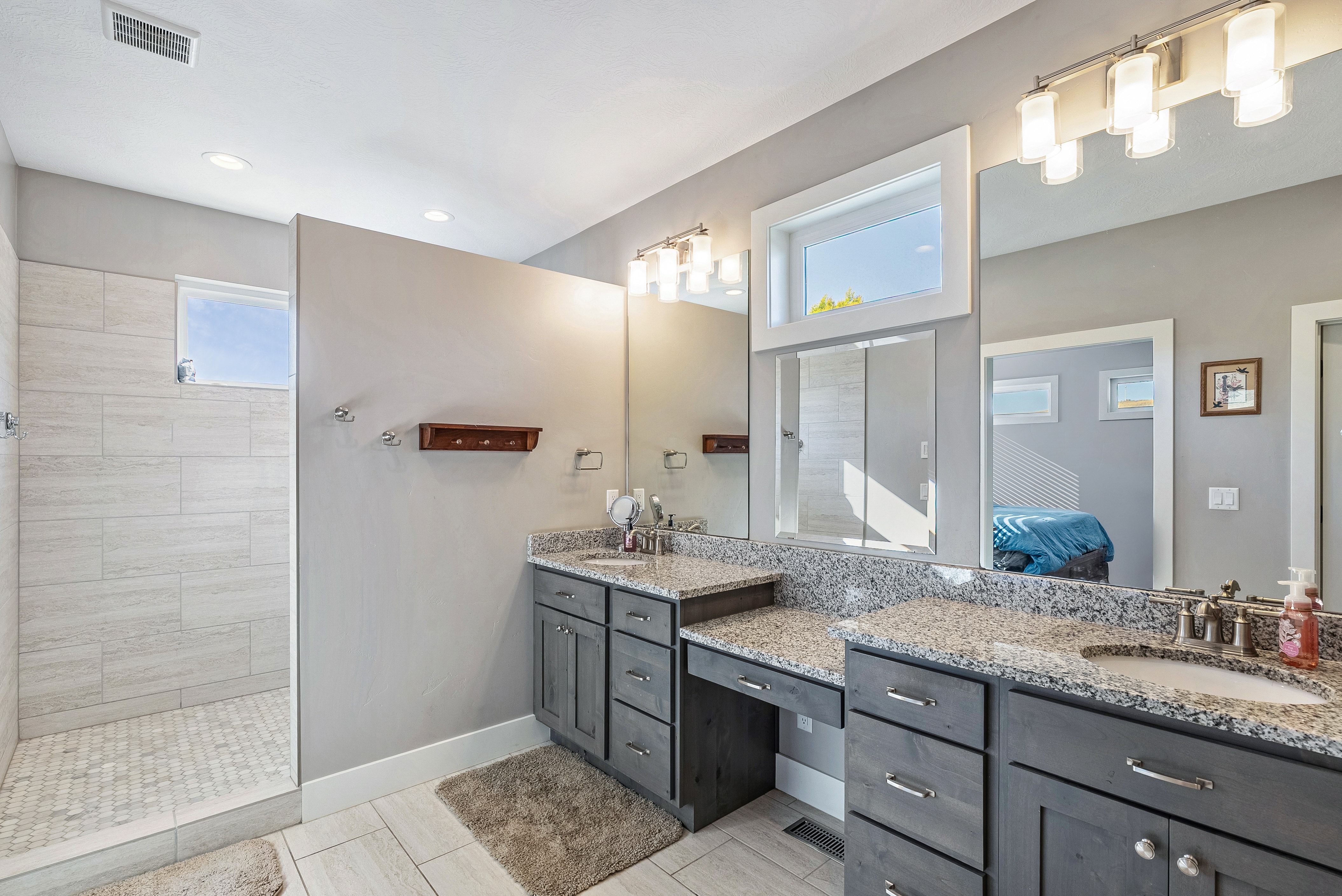 Spacious bathroom featuring a walk-in shower with light-toned tile, dual vanities with stone countertops, and dark wood cabinetry