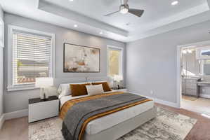 Spacious sleeping area featuring a tray ceiling with recessed lighting and a ceiling fan, two windows with horizontal blinds, and carpeted flooring