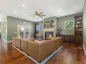 Living room featuring ceiling fan, dark wood-style flooring, a glass covered fireplace, recessed lighting, and healthy amount of natural light