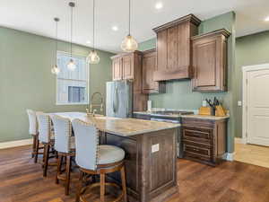 Kitchen with appliances with stainless steel finishes, dark wood-style flooring, a center island with sink, recessed lighting, and a kitchen bar