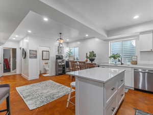 Kitchen with stainless steel dishwasher, a kitchen breakfast bar, recessed lighting, white cabinets, and a center island