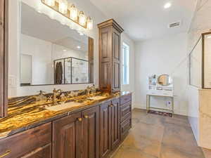Bathroom with a marble finish shower, double vanity, and recessed lighting