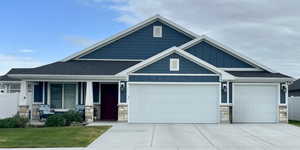 Craftsman house featuring stone siding, an attached garage, covered porch, board and batten siding, and driveway