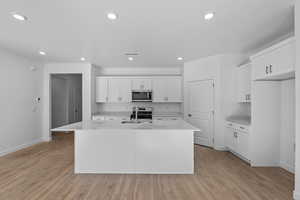 Kitchen with light countertops, an island with sink, white cabinetry, and recessed lighting