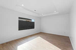 Spare room with a raised ceiling, recessed lighting, and wood finished floors