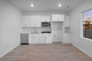 Kitchen with white cabinetry, stainless steel appliances, light countertops, recessed lighting, and light wood-style flooring