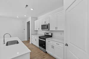Kitchen featuring stainless steel appliances, white cabinets, light countertops, recessed lighting, and light wood-style floors