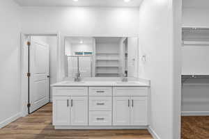 Bathroom with double vanity, a walk in closet, a shower stall, recessed lighting, and wood finished floors