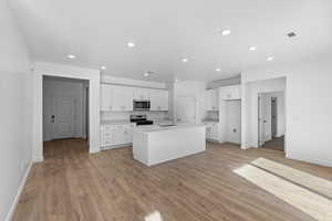 Kitchen featuring white cabinetry, recessed lighting, stainless steel appliances, an island with sink, and light wood finished floors