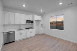 Kitchen featuring stainless steel appliances, light wood-type flooring, white cabinets, light countertops, and recessed lighting